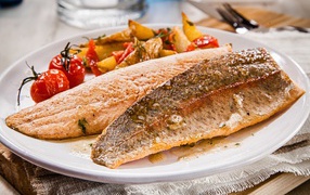Baked fish with tomatoes and vegetables on a white plate
