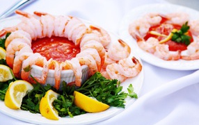 Вареные креветки с соусом на тарелке с лимоном и зеленью петрушки 