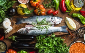 Свежая рыба на столе с овощами и зеленью 