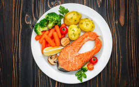 Красная рыба с овощами на белой тарелке на столе