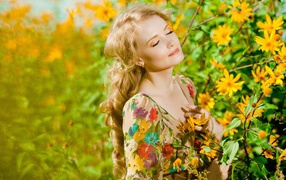 A beautiful blonde is basking in the sun at the yellow flowers