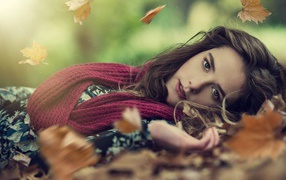 Красивая шатенка в красном шарфе лежит на сухой листве