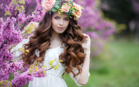 A beautiful brown-haired woman in a white dress with a wreath of roses on her head