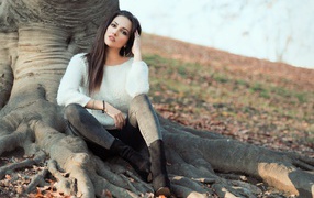 A beautiful girl is sitting near a tree