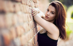 Нежная  девушка шатенка стоит у кирпичной стены