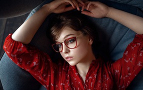 Молодая девушка в очках лежит на диване 