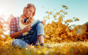 A young girl is reading a book on a yellow grass in the fall