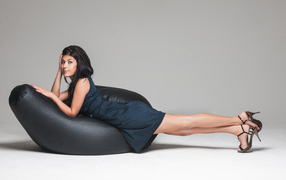 Молодая девушка лежит в черном платье на черном кресле 