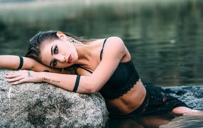 Молодая девушка с татуировками сидит у камня в воде