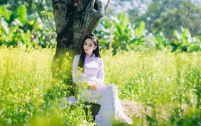 Красивая девушка азиатка сидит в белом платье под деревом