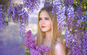 Beautiful blonde with a bouquet of lilac on the background of wisteria flowers