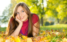 Beautiful blue-eyed brown-haired woman lies on the grass with yellow leaves