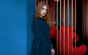 Красивая голубоглазая девушка стоит в пальто у стены