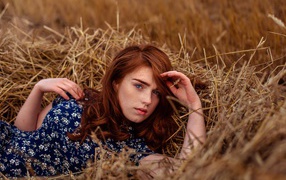 Красивая голубоглазая рыжеволосая девушка лежит в сене