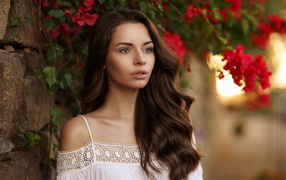Beautiful brown-haired woman near the wall on a background of red flowers