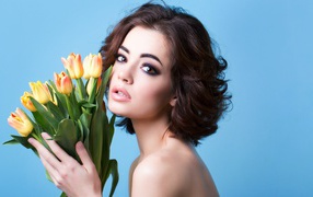Красивая девушка брюнетка с букетом тюльпанов на голубом фоне