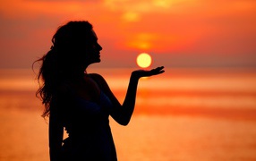 Красивая девушка держит солнце в ладони на закате