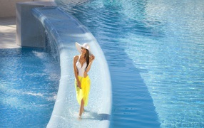 Красивая девушка в купальнике и большой белой шляпе идет по воде