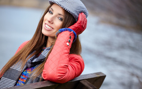 Красивая девушка в красной куртке сидит на лавке
