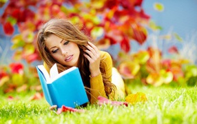 Красивая девушка читает книгу лежа на зеленой траве