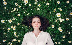 Beautiful girl lies on green grass with daisies
