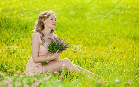 Красивая девушка с букетом сидит на зеленой траве