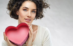 Beautiful girl with a box in the shape of a heart in hands on a gray background