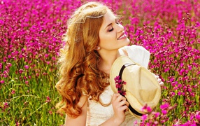 Beautiful girl with hat in hands on a field with pink flowers