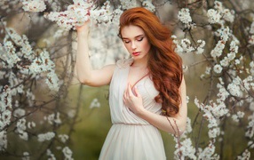 Beautiful red-haired girl by the flowering apricot tree