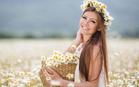 Красивая улыбающаяся девушка на поле с корзиной ромашек