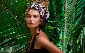 Красивая женщина в тюрбане с украшениями среди зеленых пальмовых листьев