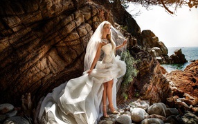 Девушка невеста в белом платье стоит на камнях у скалы