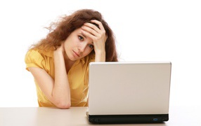 Грустная девушка сидит возле ноутбука 