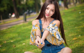 Улыбающаяся девушка азиатка сидит на траве