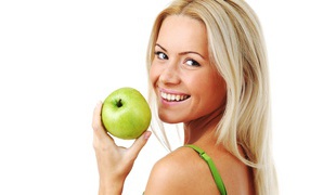 Улыбающаяся девушка блондинка с зеленым яблоком в руке на белом фоне