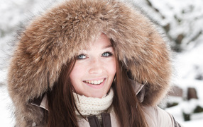 Улыбающаяся голубоглазая девушка в капюшоне зимой