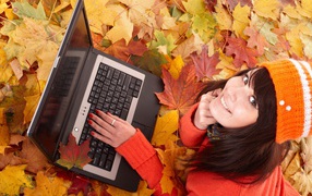 Девушка лежит на сухой опавшей листве с ноутбуком осенью