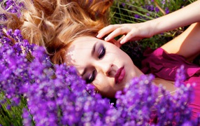 Young beautiful girl lying on the grass with lilac flowers
