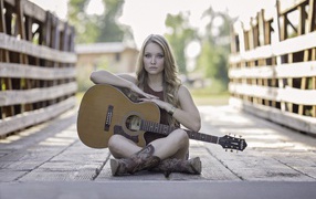 Молодая девушка блондинка сидит на мосту с гитарой