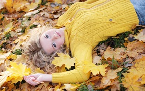 Молодая блондинка лежит на сухой листве осенью