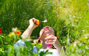 Молодая девушка лежит на зеленой траве с мыльными пузырями