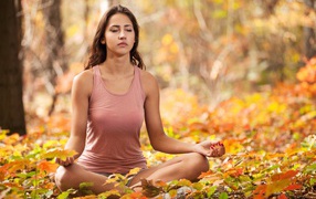 Молодая девушка медитирует в лесу сидя на земле