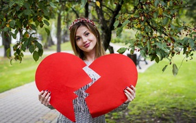 Молодая девушка с разбитым красным сердцем в руках