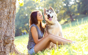 Young girl with husky sitting under a tree in summer