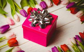 Красная коробка с подарком на столе с тюльпанами