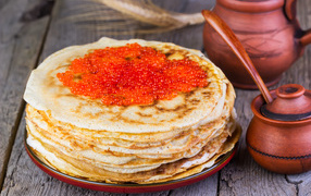 A pile of pancakes with red caviar on a wooden table, a treat for Shrovetide
