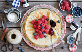 Тонкие блины с малиной и черникой на столе вид сверху
