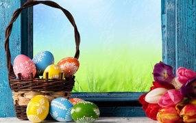 Пасхальные яйца в корзине на подоконнике с букетом тюльпанов