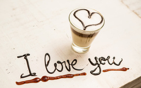 A glass of coffee with a heart and an inscription of chocolate I love you on the table