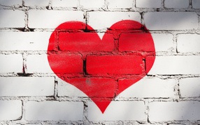 A large red heart is painted on a brick wall